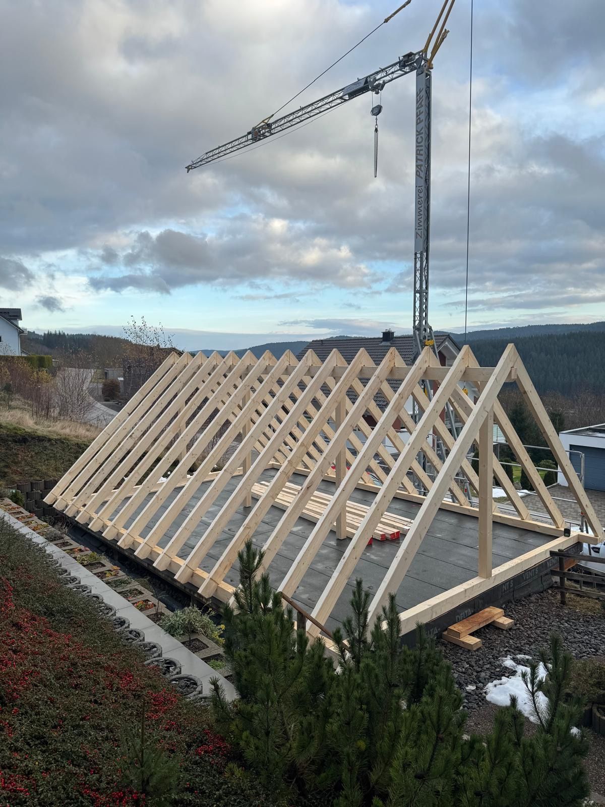 Eine Baustelle mit einem Kran, der ein Stück Holz anhebt, Zimmerei Patrick Pfaff