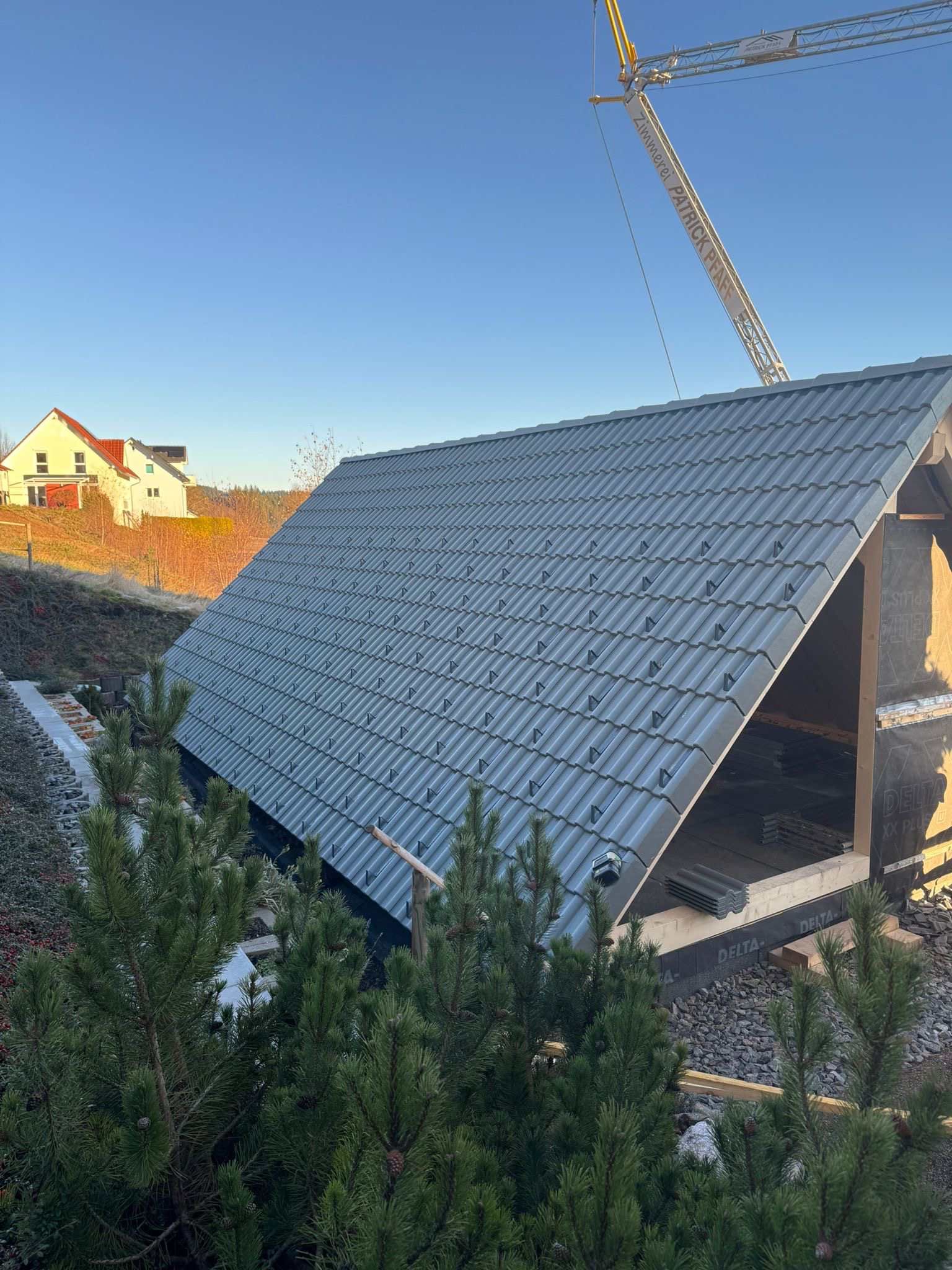 Eine Baustelle mit einem Kran, der ein Stück Holz anhebt, Zimmerei Patrick Pfaff