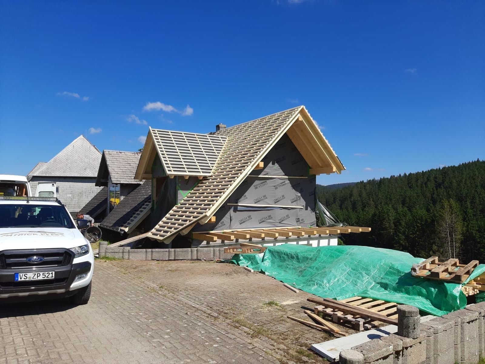 Eine Baustelle mit einem Kran, der ein Stück Holz anhebt, Zimmerei Patrick Pfaff