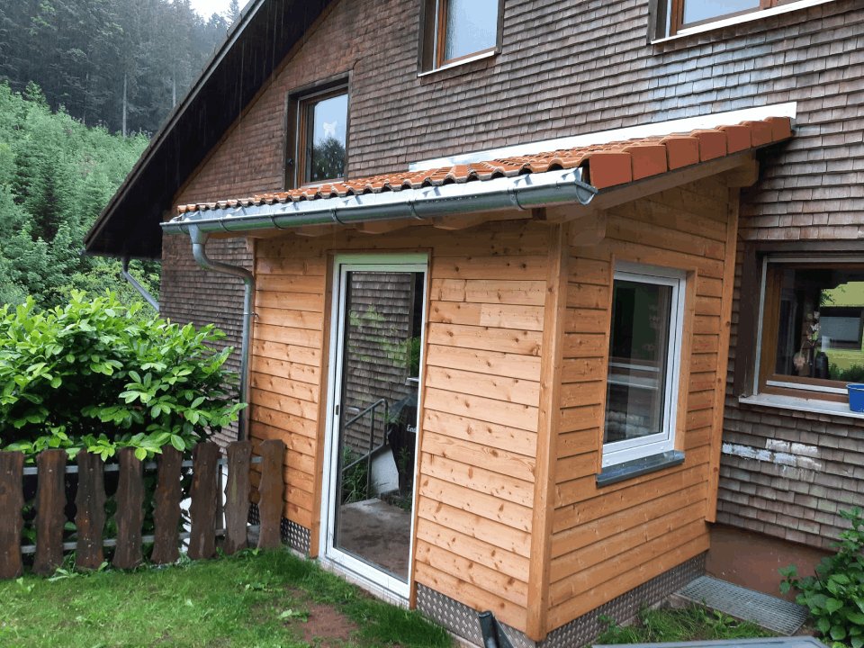 Ein Holzhaus mit einem Zaun davor, Zimmerei Patrick Pfaff