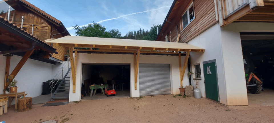 Eine Garage mit Holzdach steht neben einem Haus, Zimmerei Patrick Pfaff