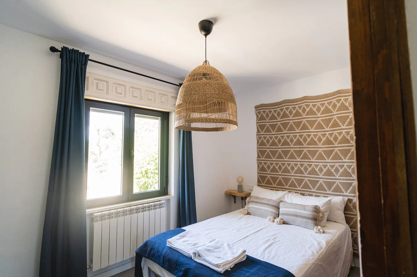 Un dormitorio con una cama, ventana, cortinas y una lámpara colgando del techo.