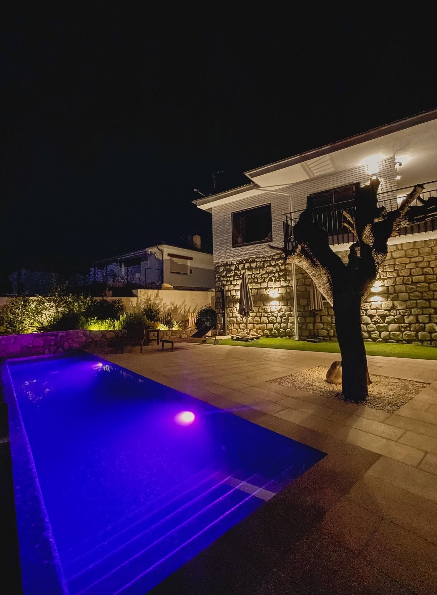 Una gran piscina está iluminada por la noche frente a una casa.