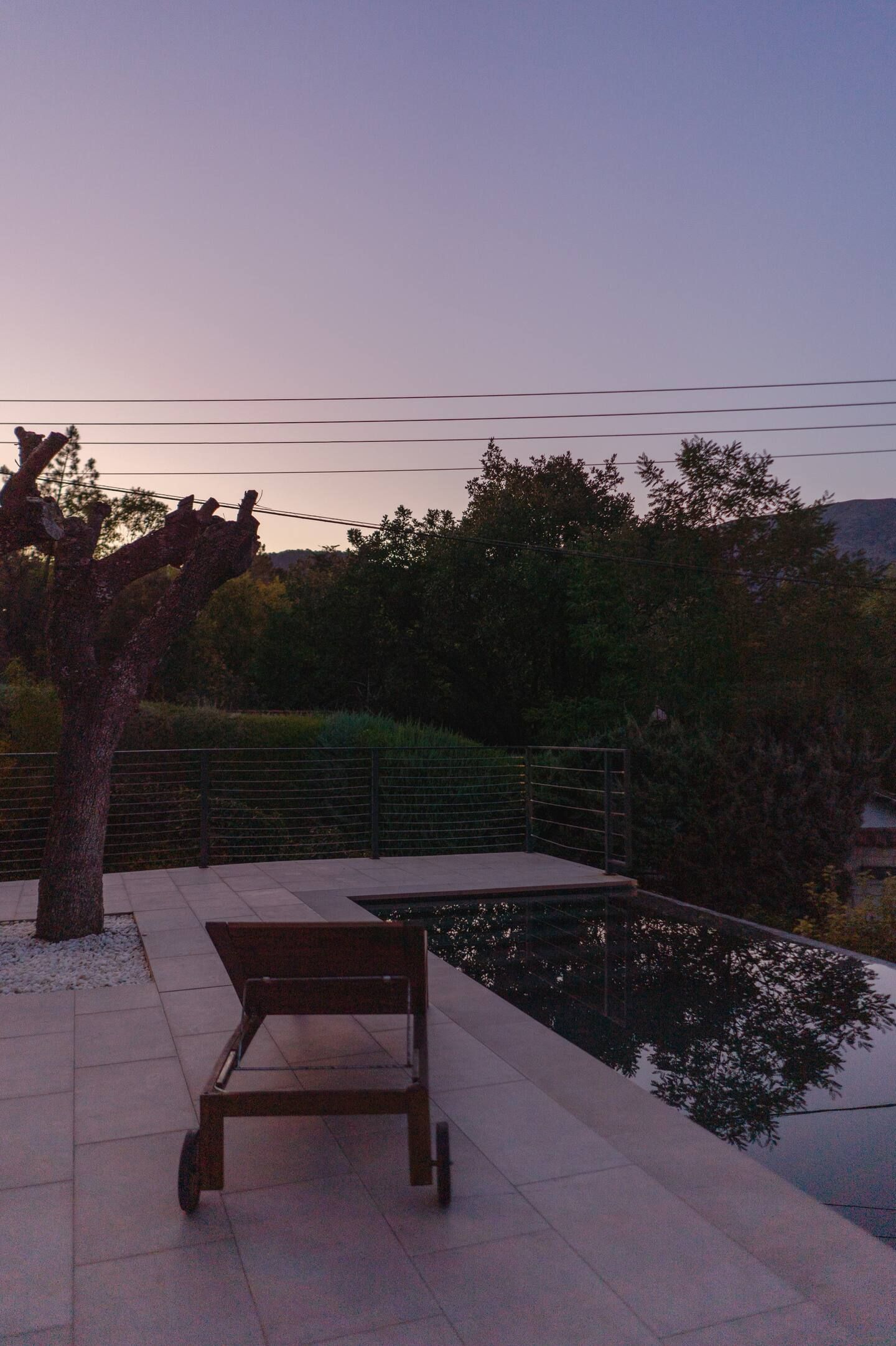 Una puesta de sol sobre una piscina con una silla en primer plano.