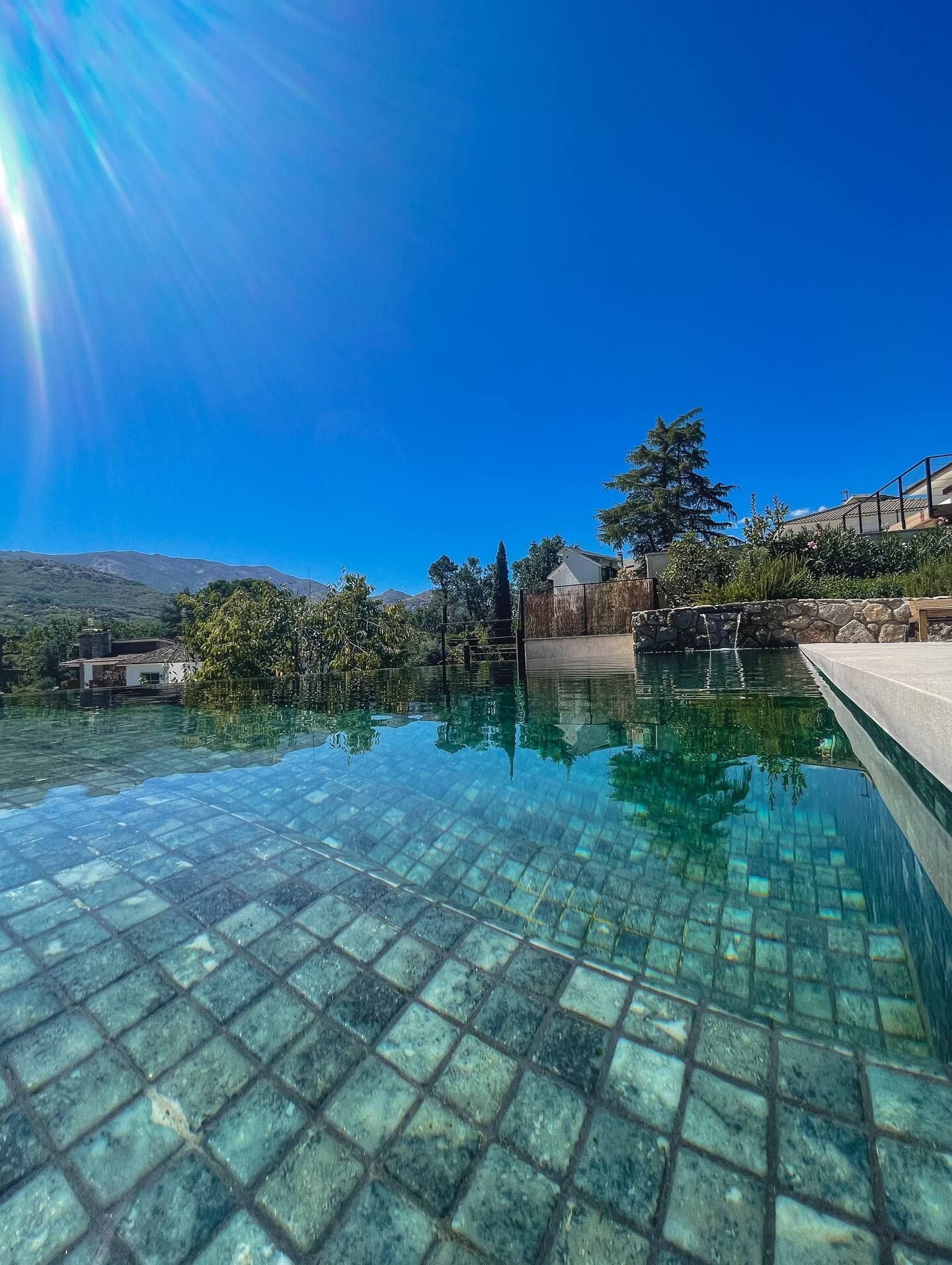 Una gran piscina rodeada de árboles y montañas en un día soleado.