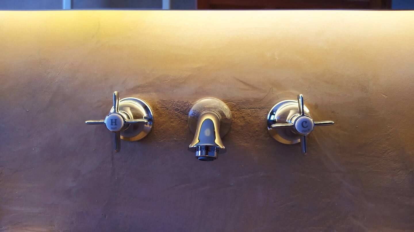 Un lavabo de baño con tres grifos y una luz en la pared.