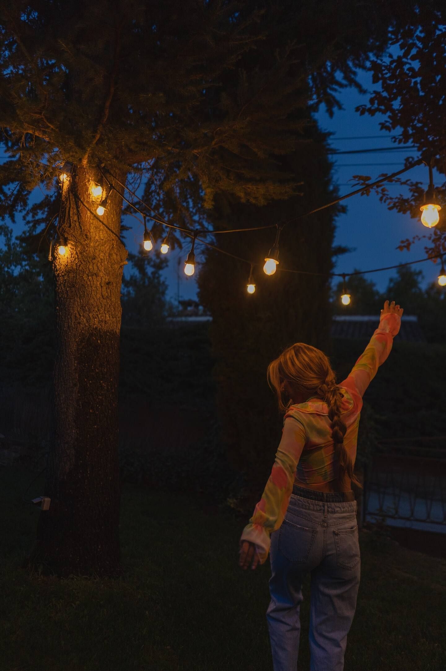 Una mujer está parada debajo de un árbol con los brazos extendidos en la noche.