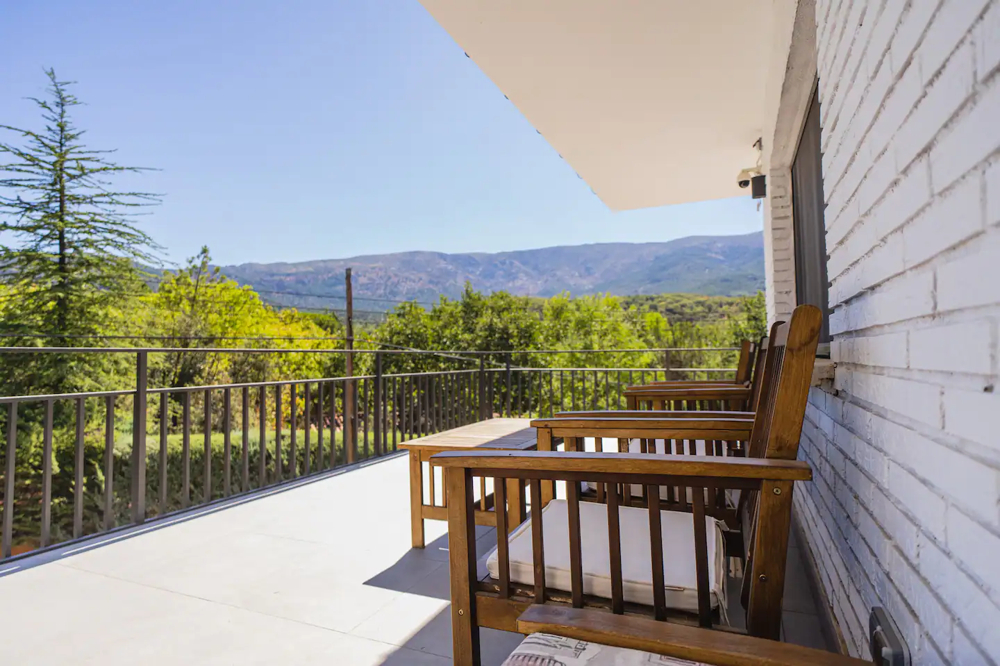Un balcón con sillas de madera y vista a las montañas.