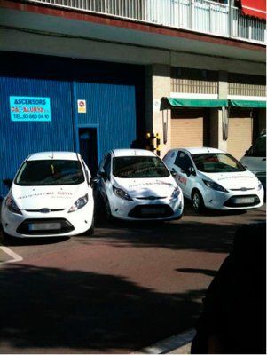 Tres coches blancos están aparcados delante de un edificio azul.