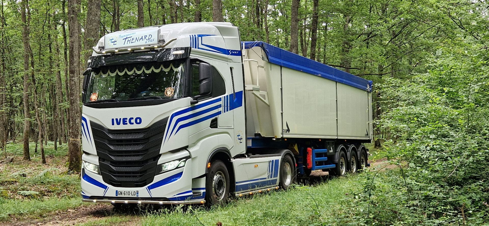 Un semi-remorque Iveco blanc est garé sur un chemin forestier