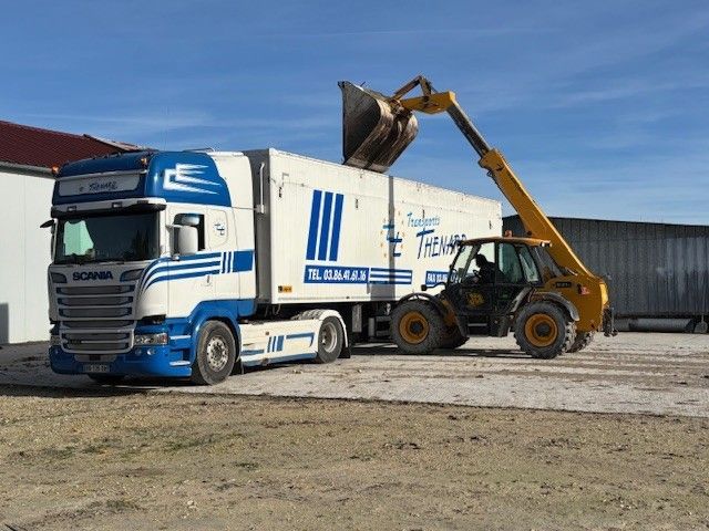 Un camion-benne blanc et bleu est chargé par une excavatrice jaune dans une gravière
