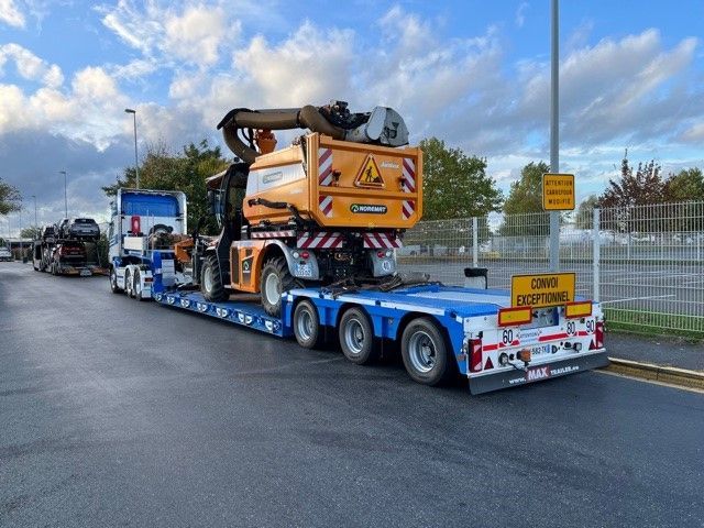 Un camion plateau bleu transporte une excavatrice jaune sur une route