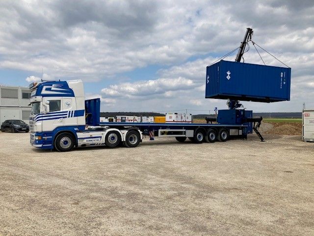 Camion-grue bleu soulevant un conteneur maritime bleu dans une cour