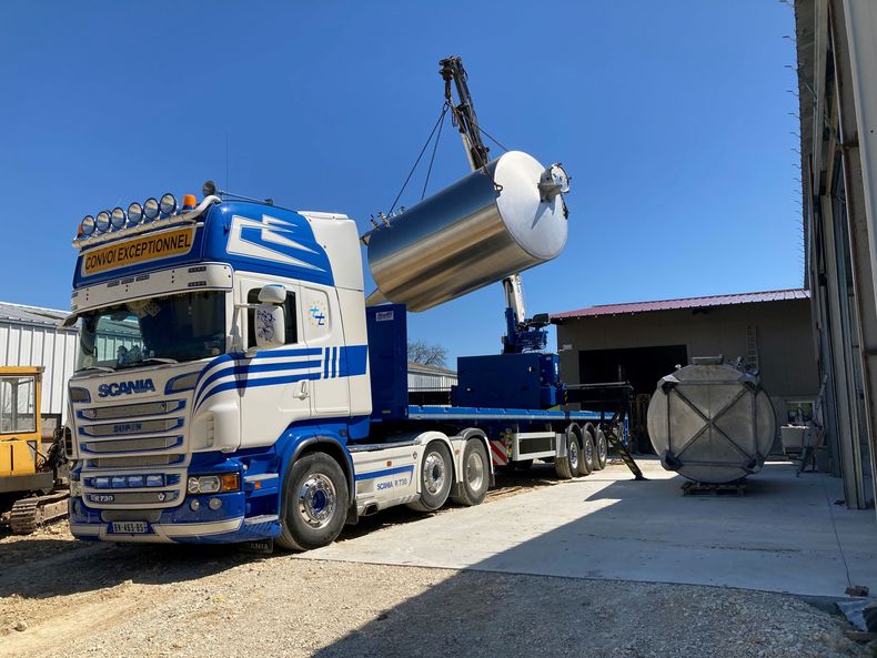 Camion bleu et blanc transportant une grande cuve métallique sur un site industriel