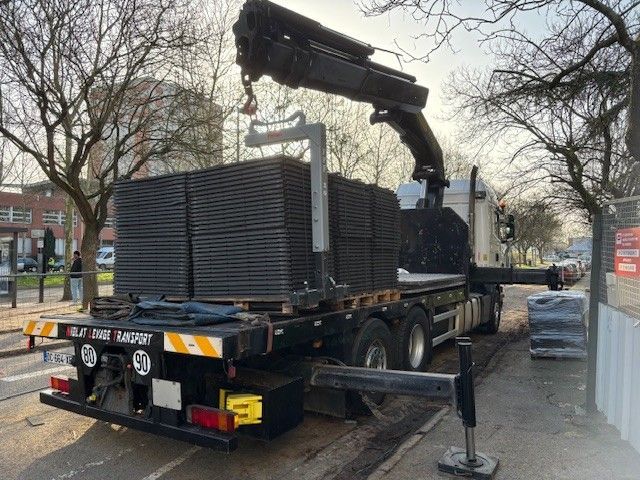 Grue montée sur camion chargeant des panneaux noirs empilés sur une plateforme