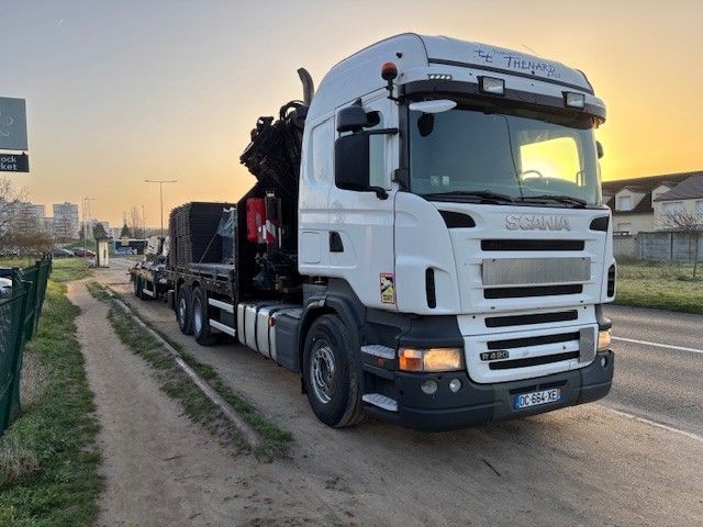 Camion Scania blanc transportant du matériel lourd en bord de route au coucher du soleil