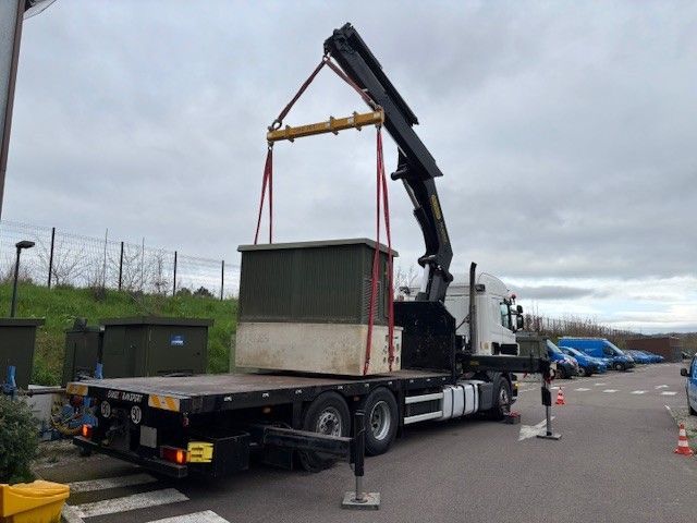 Une grue charge un grand conteneur sur un camion plateau dans une zone industrielle.
