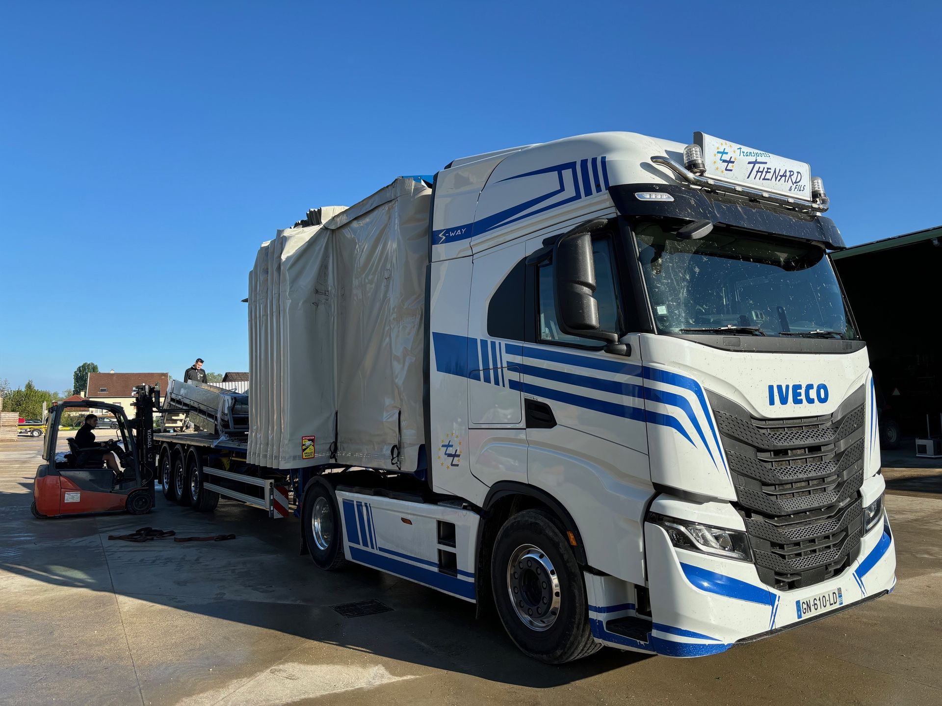 Un semi-remorque Iveco blanc transportant une cargaison bâchée sur une remorque à plateau