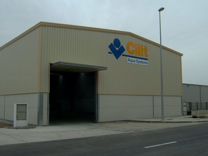 Edificio industrial de color beige con gran puerta abierta y logotipo azul