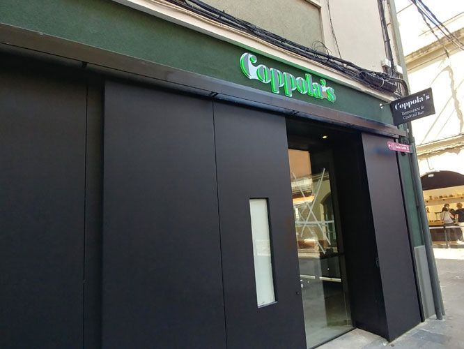 Fachada de Coppola con puertas corredizas negras, letrero verde y un pequeño cartel. Exterior del edificio.