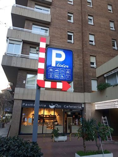 Señal de estacionamiento con una flecha apuntando a la derecha, cerca de una panadería y un edificio alto.