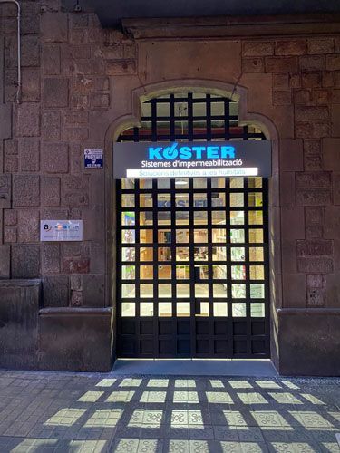 Entrada de una tienda con un cartel que dice "KÖSTER". La puerta está dividida en varios cuadrados.