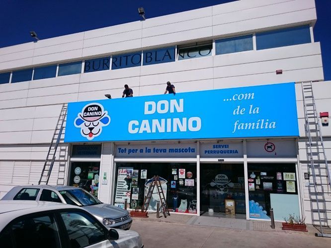 Vista exterior de una tienda de mascotas, "Don Canino", con trabajadores instalando un letrero azul.