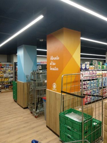 Columnas con letreros en un pasillo de un supermercado. Un letrero dice "Alimenta el bien ser" con un degradado naranja.