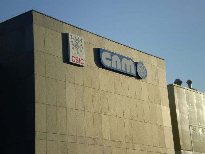 Exterior del edificio del CNM, con el logotipo del CSIC. Fachada de piedra beige, letrero azul del CNM y logotipo del reloj.