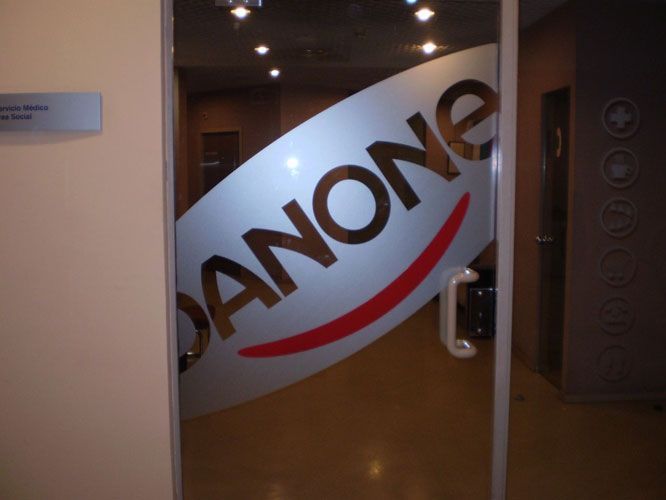 Puerta de cristal con el logotipo de Danone en un entorno corporativo.