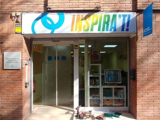 Fachada de tienda “INSPIRA’T!” con puertas de cristal, cartel con logo colorido y estanterías de exposición.
