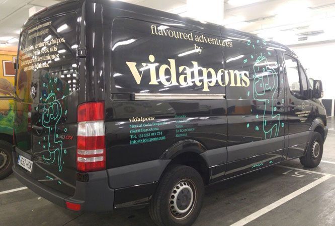Furgoneta negra con logotipo "vidatpons" y diseño verde azulado, estacionada en el interior.