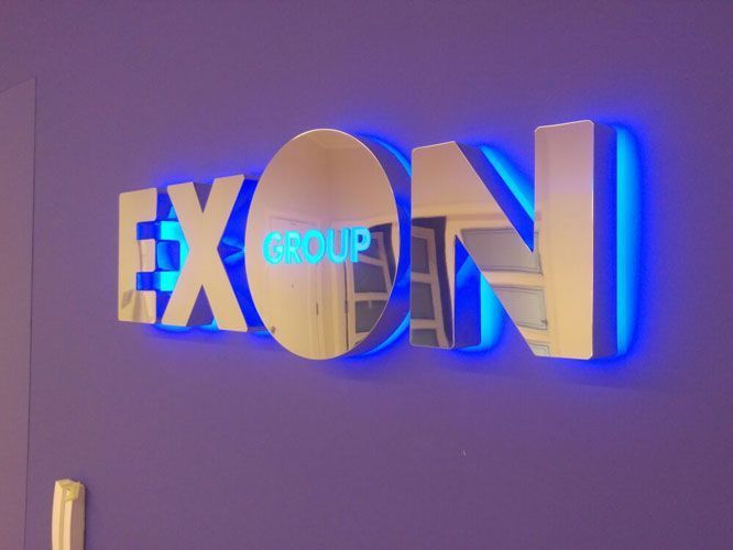 Letrero brillante "EXON GROUP" con retroiluminación azul sobre una pared violeta.