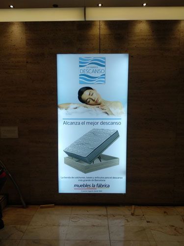 Anuncio de colchones Descanso; mujer relajándose, con el colchón expuesto. Fondo azul claro, texto blanco.