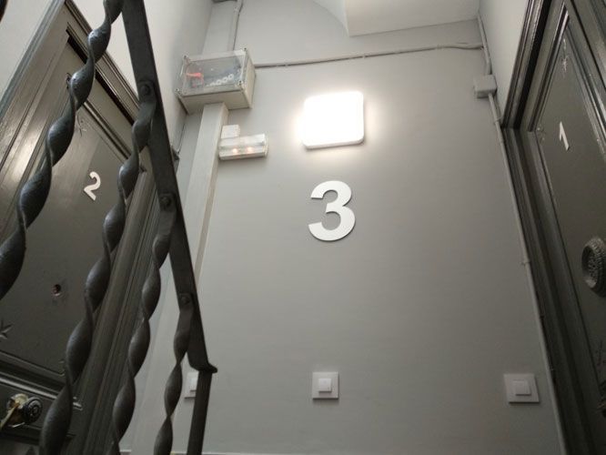 Puertas de apartamento 1, 2 y 3 en una pared gris con luz e interruptores. Barandilla metálica en primer plano.