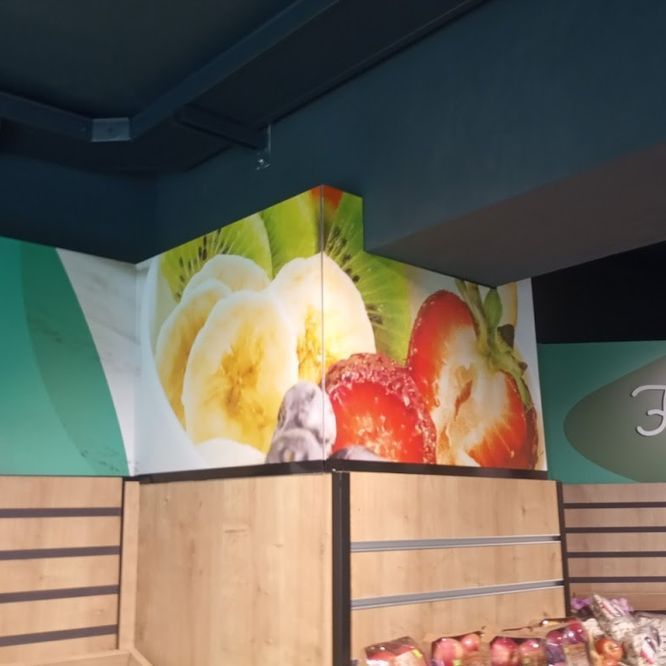 Exhibición de frutas: plátanos, kiwis y fresas en la pared de un mercado. Exhibición de madera debajo.