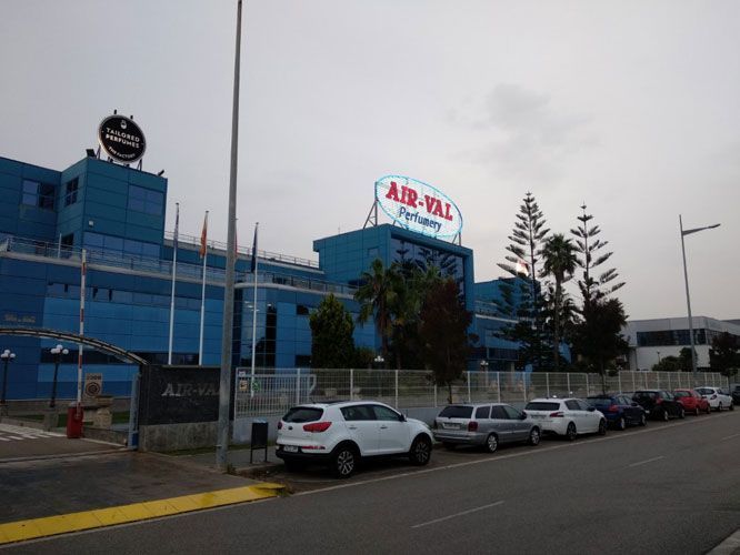 Edificio de la fábrica Air-Val de color azul con logotipo en el techo y automóviles estacionados en el frente.