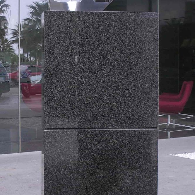 Pilar de granito negro al aire libre, con superficie reflectante junto a ventanas de vidrio.