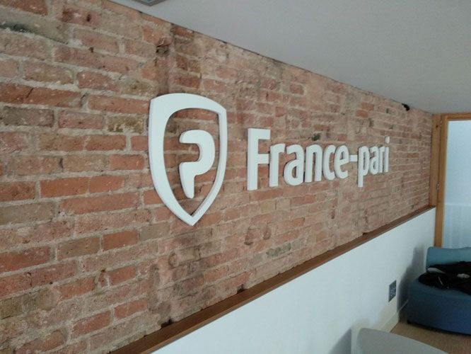 Logotipo de France-Pari en una pared de ladrillos; escudo y texto blancos.