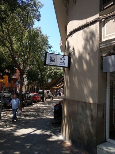 Letrero en esquina de edificio en una calle con una persona, autos y árboles.