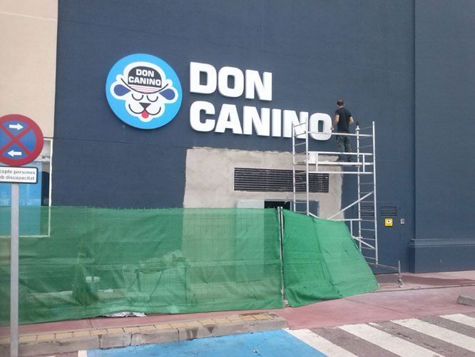 Cartel de "Don Canino" con una persona en un andamio realizando trabajos de construcción.