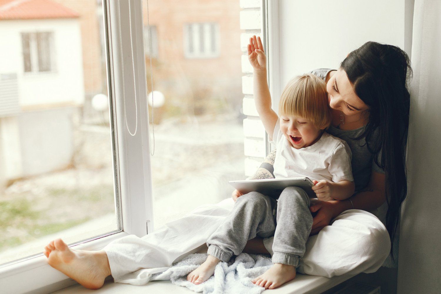 Enfant qui regarde une tablette avec sa mère à côté d'une baie vitrée