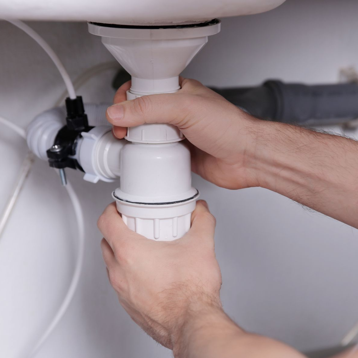 Des mains assemblent un siphon en plastique blanc sous un évier.