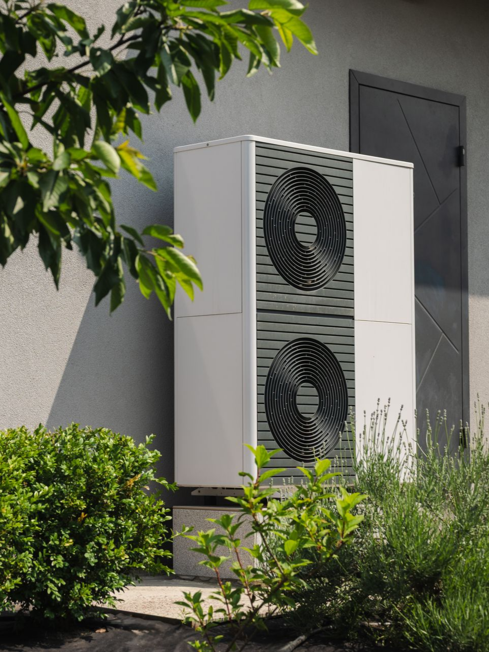 Unité de pompe à chaleur blanche avec grille circulaire, près d'une maison entourée de verdure.