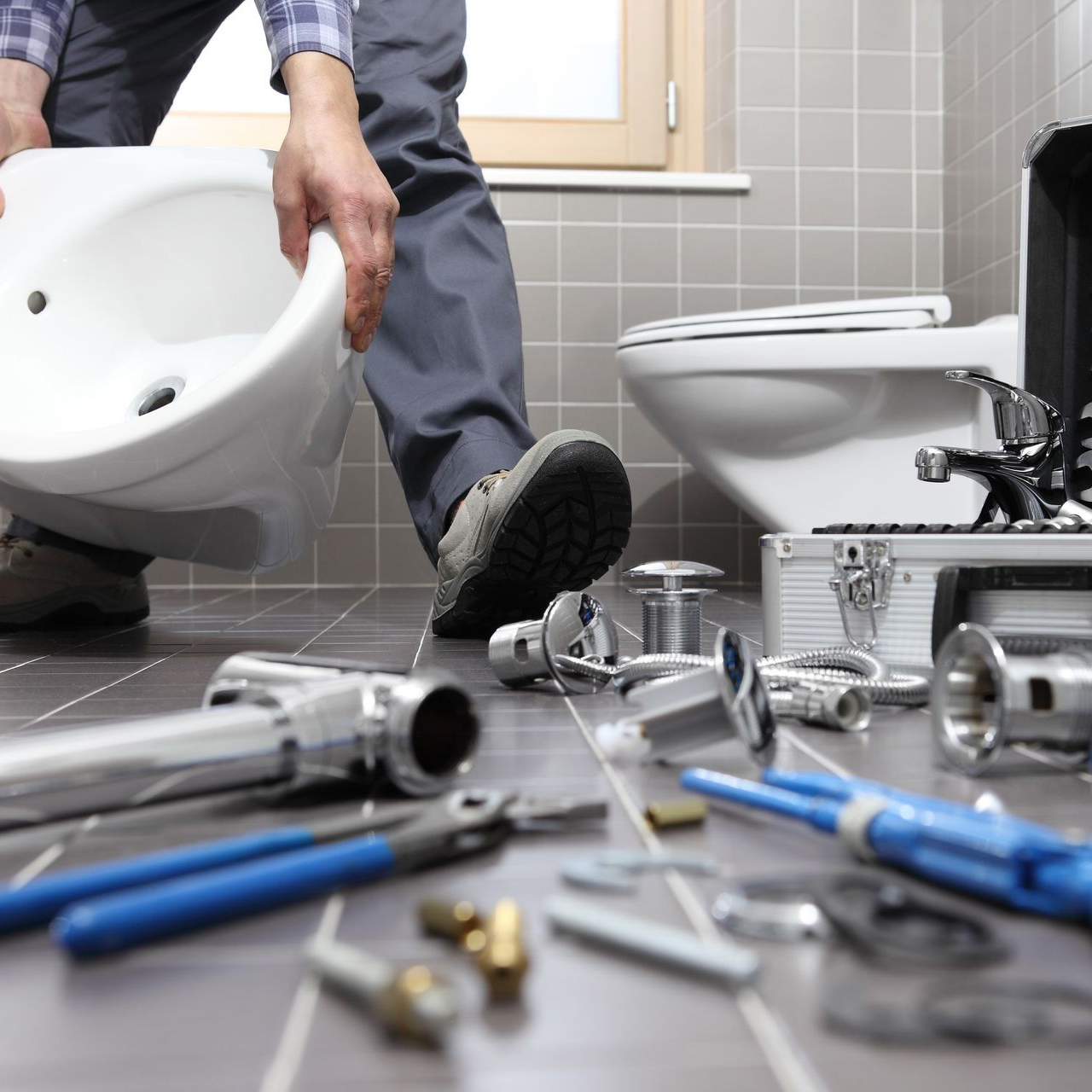 Un plombier installe un bidet dans une salle de bains, entouré d'outils et d'un WC.