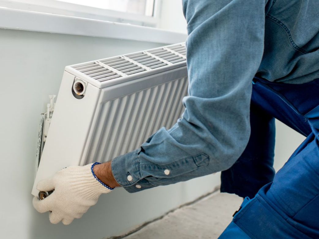 Une personne installe un radiateur blanc sur un mur.