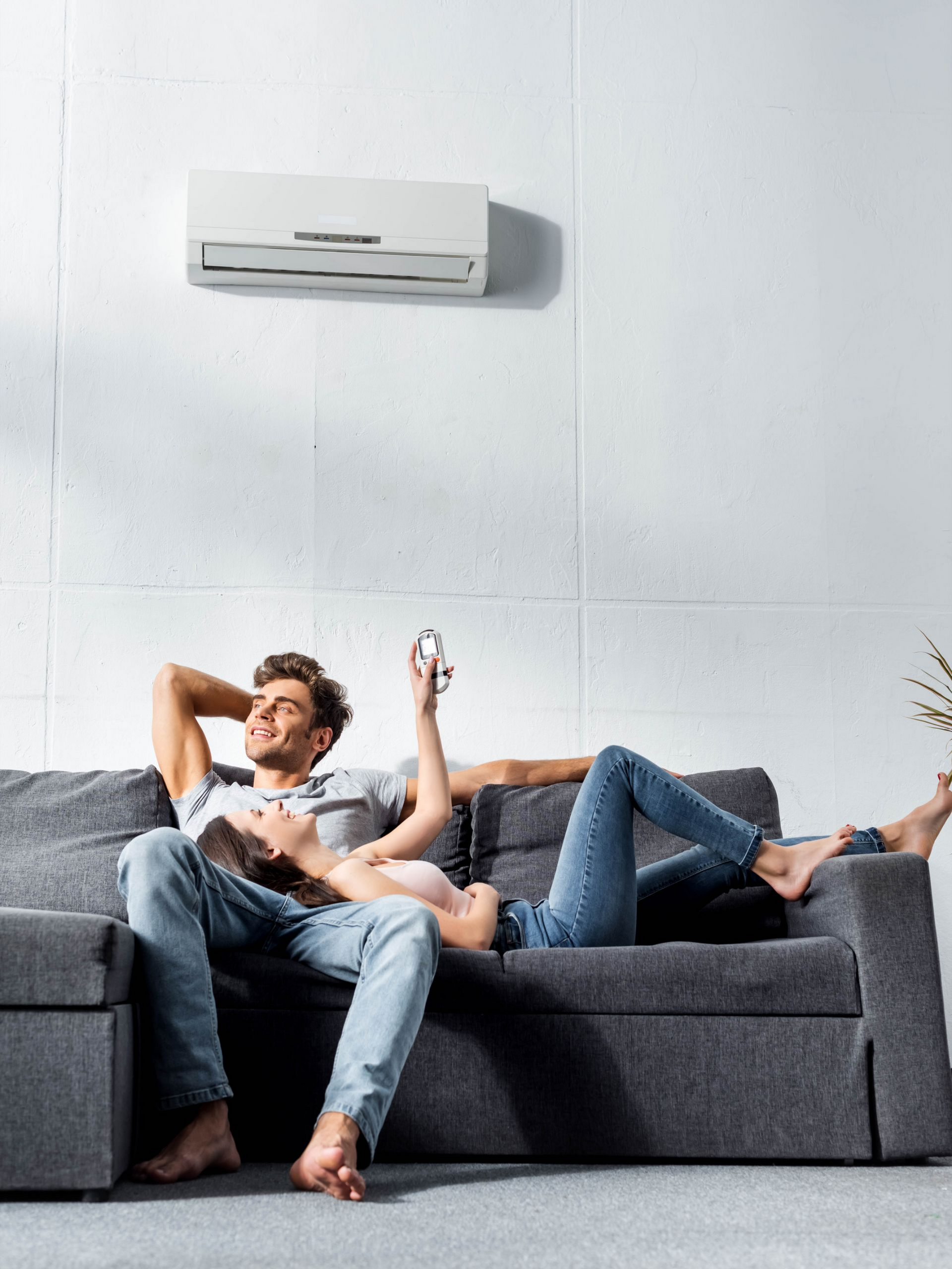 Un couple se détend sur un canapé gris sous un climatiseur.