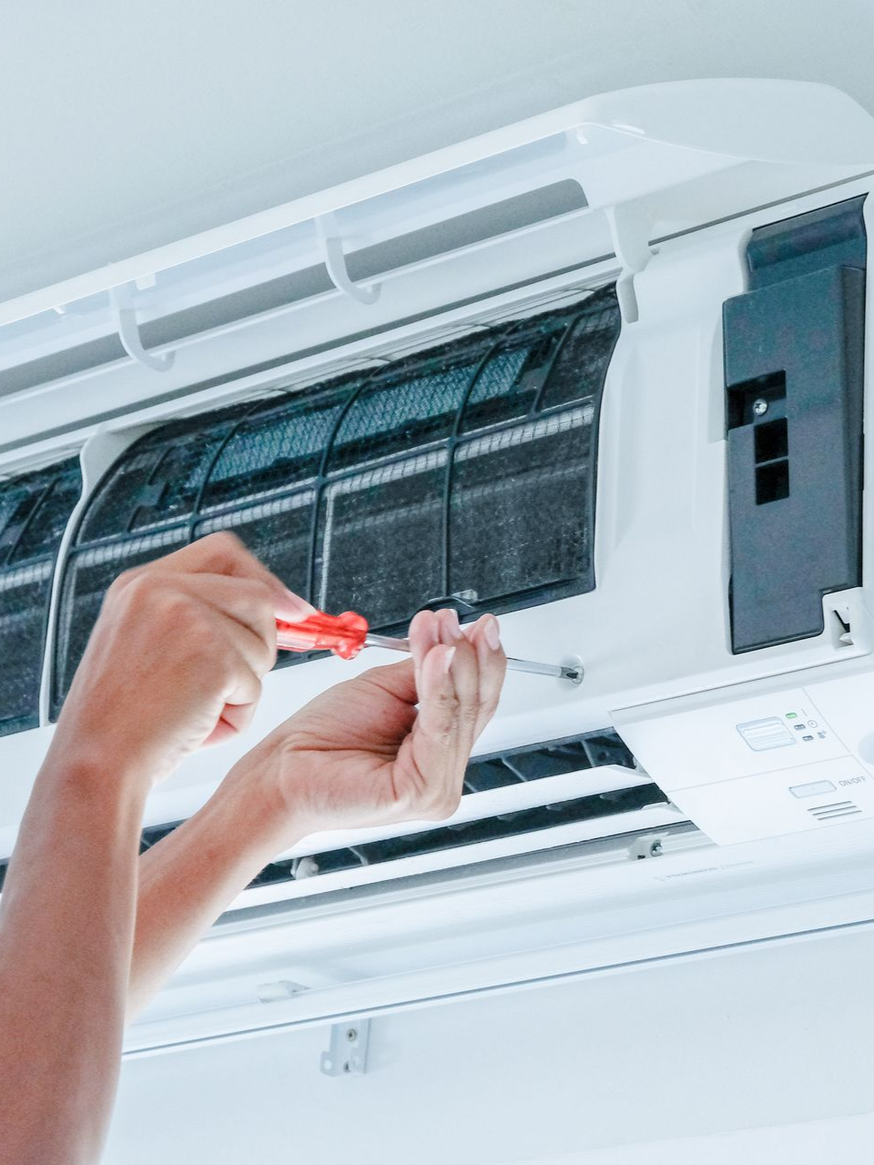 Une personne utilise un tournevis pour réparer un climatiseur mural blanc.