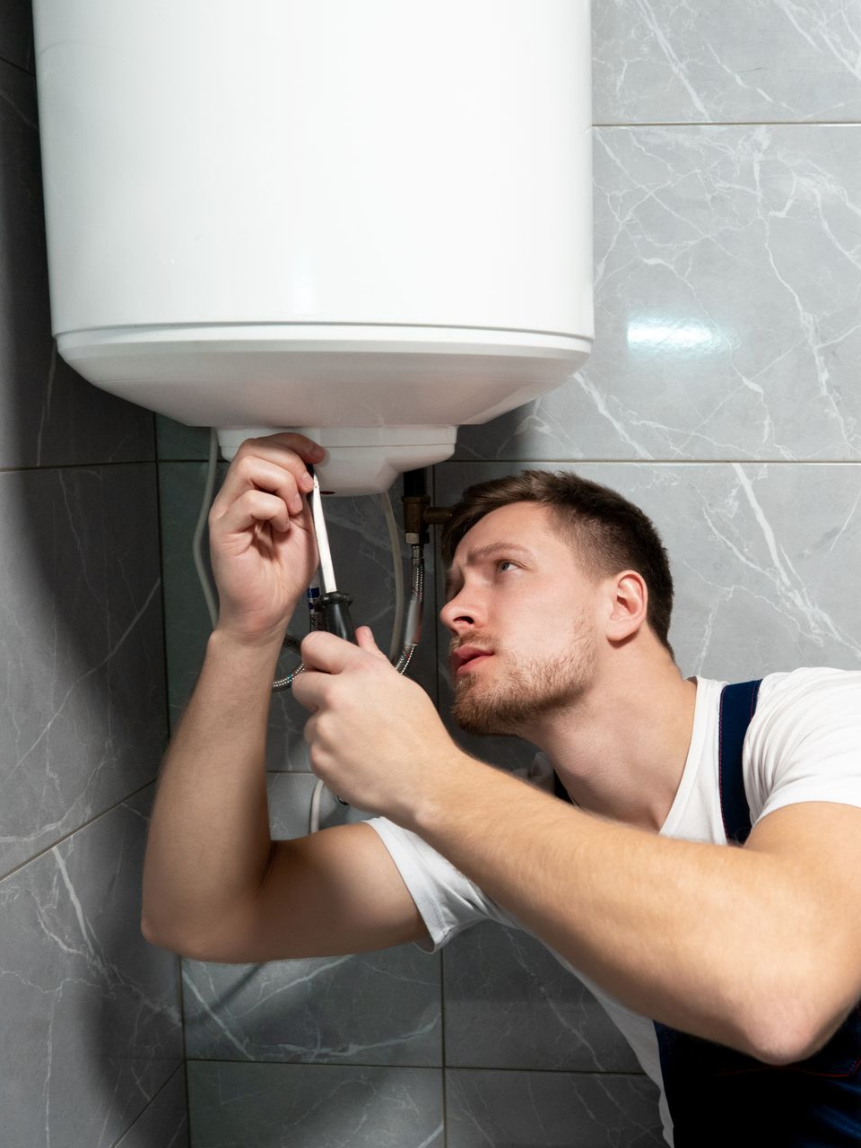 Un homme utilise un tournevis pour réparer un chauffe-eau.