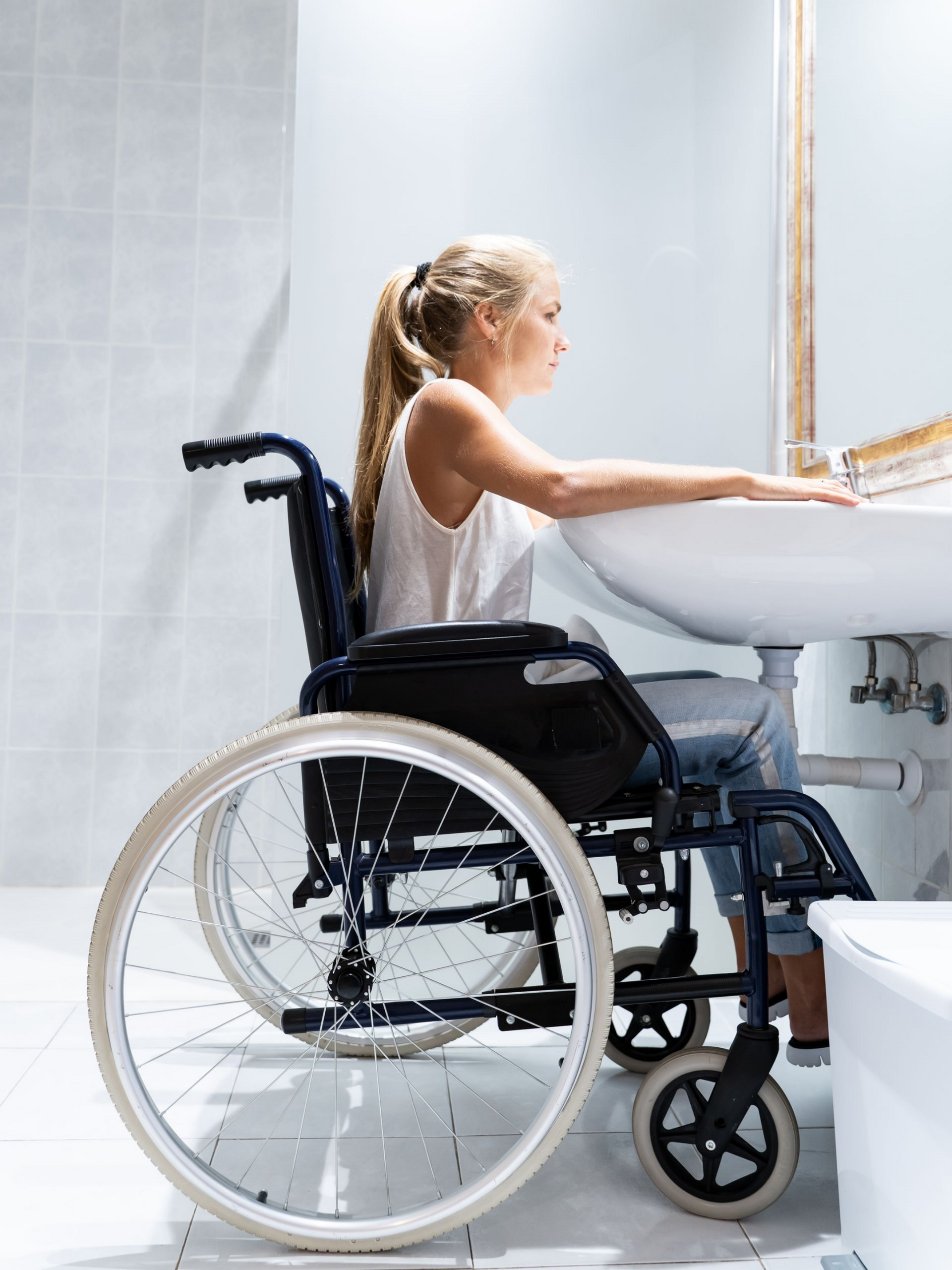 Une jeune fille assise dans un fauteuil roulant face à un lavabo.